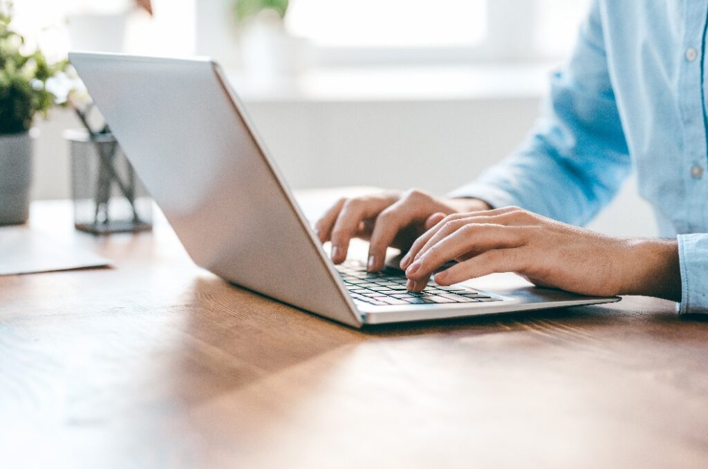 Die Hände eines jungen, modernen Büroleiters über der Tastatur seines Laptops während der Arbeit